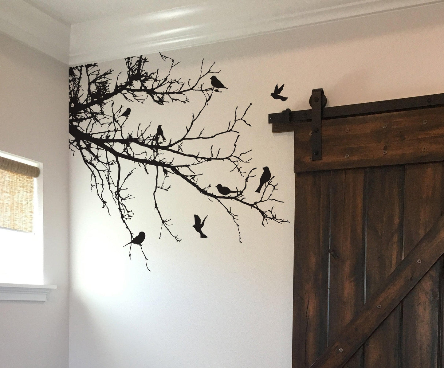 Black decal of 8 birds on tree branches on a white wall near a wooden door.