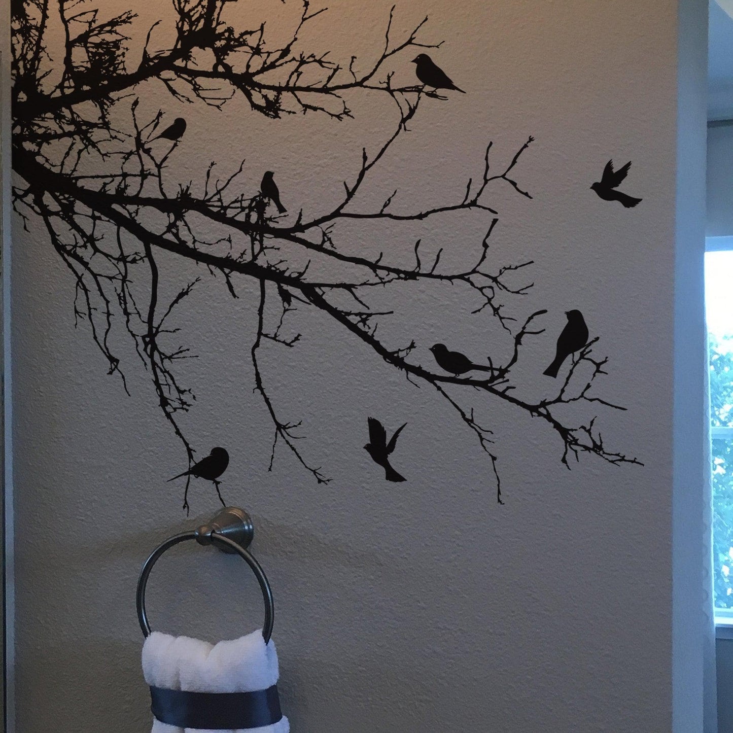 Black decal of 8 birds on tree branches on a white wall above a towel.