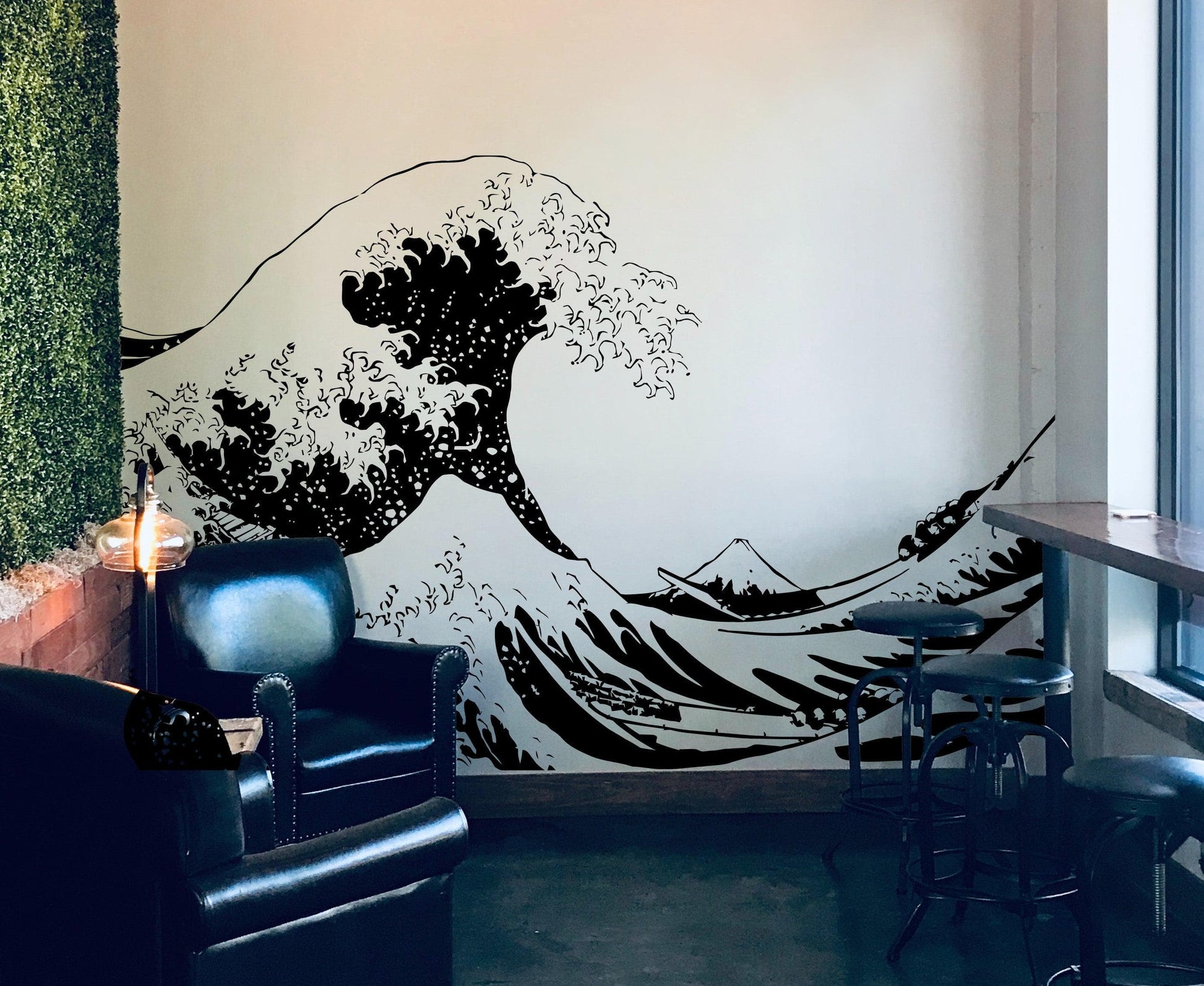 The Great Wave wall decal on a white wall near black couches and stool chairs.