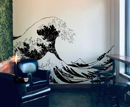 The Great Wave wall decal on a white wall near black couches and stool chairs.