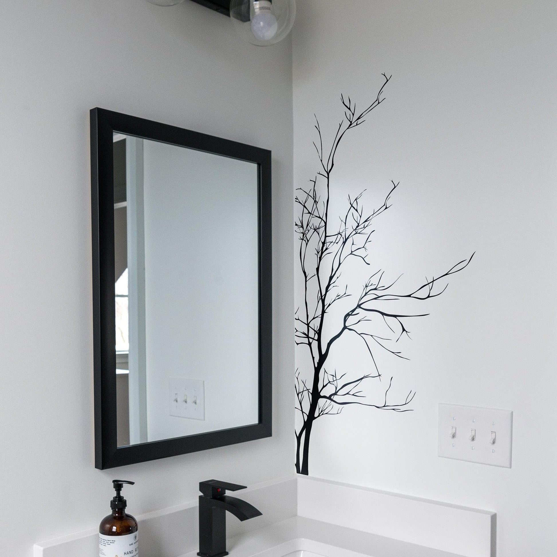 A black tree decal on a white wall in a bathroom near a mirror.