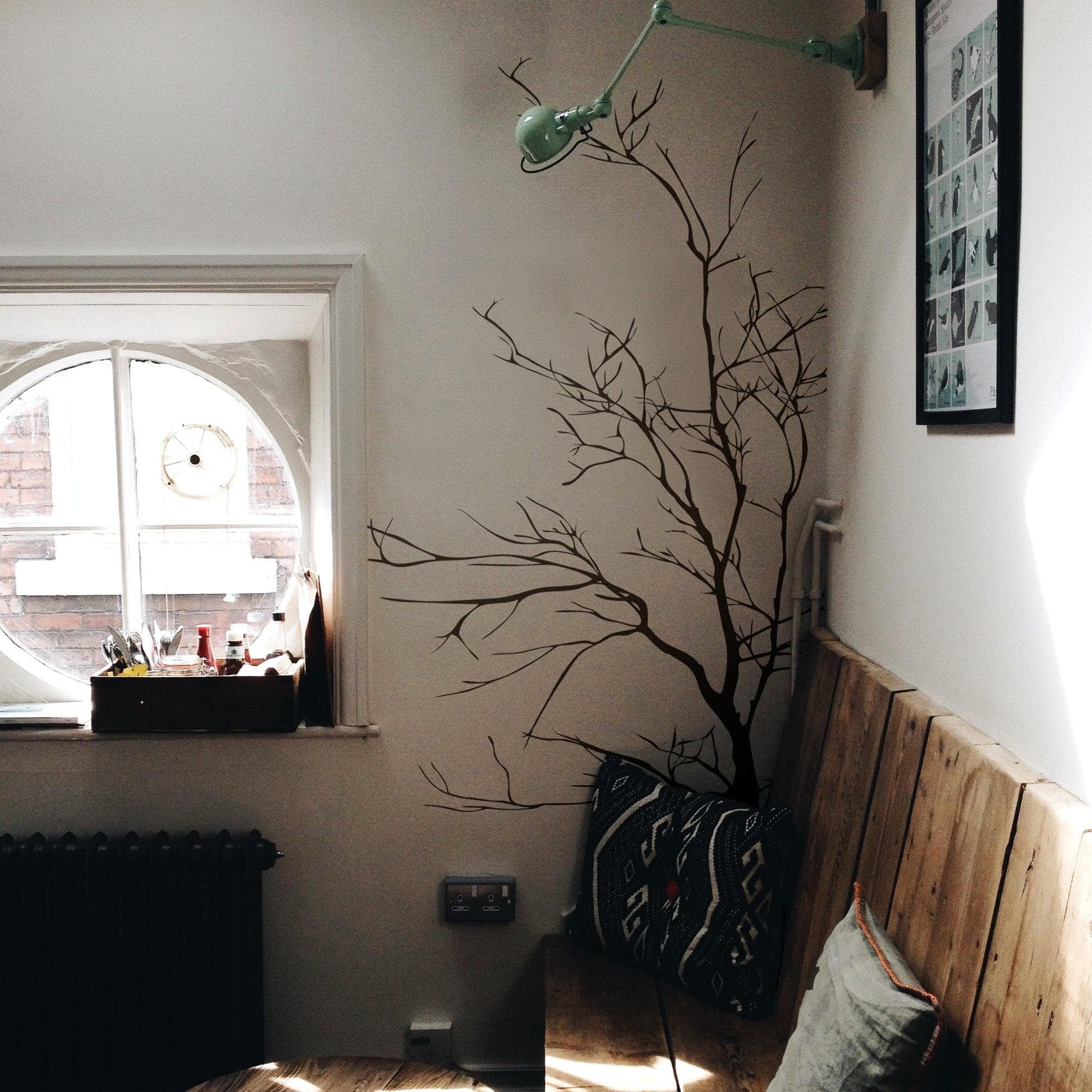 A black tree decal on a white wall near a wooden bench and circular window.