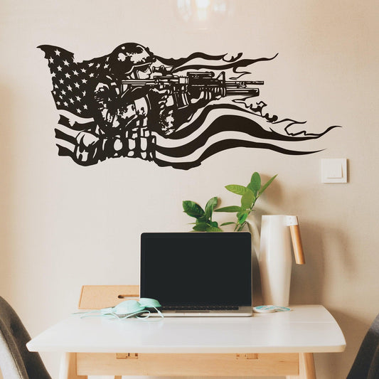 A black decal on a white wall showing a soldier holding a gun and the American flag behind it. Underneath it is a desk with a laptop.