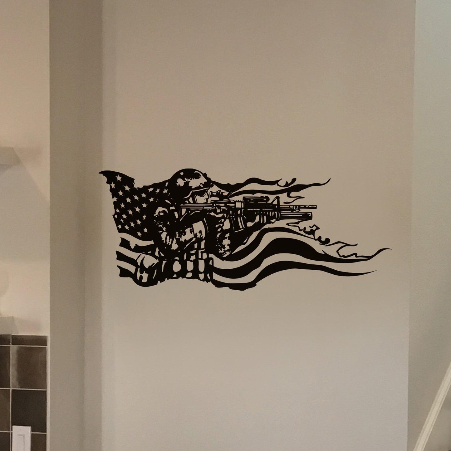 A black decal on a white wall showing a soldier holding a gun and the American flag behind it. 