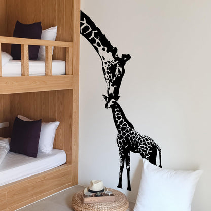 A black adult giraffe and a young giraffe decal on a white wall in a bedroom.