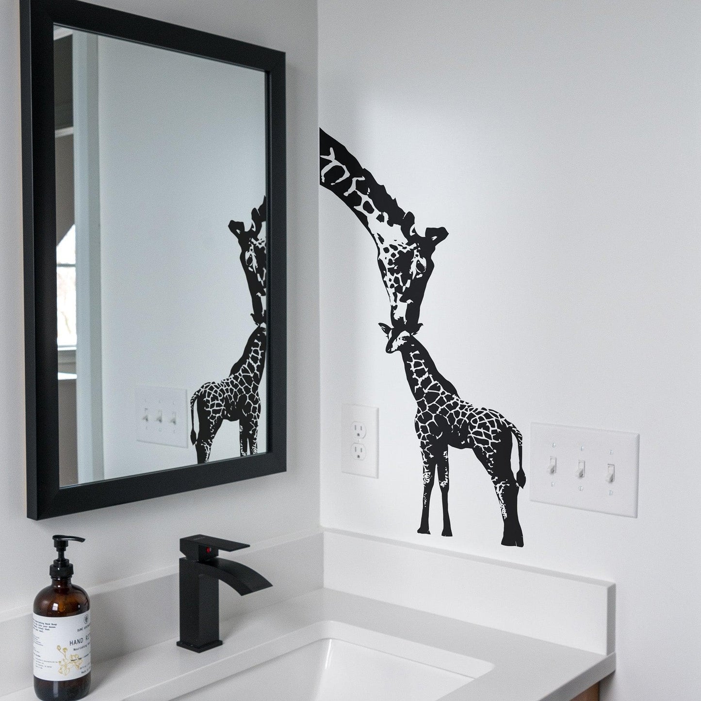 A black adult giraffe and a young giraffe decal on a white wall in a bathroom.