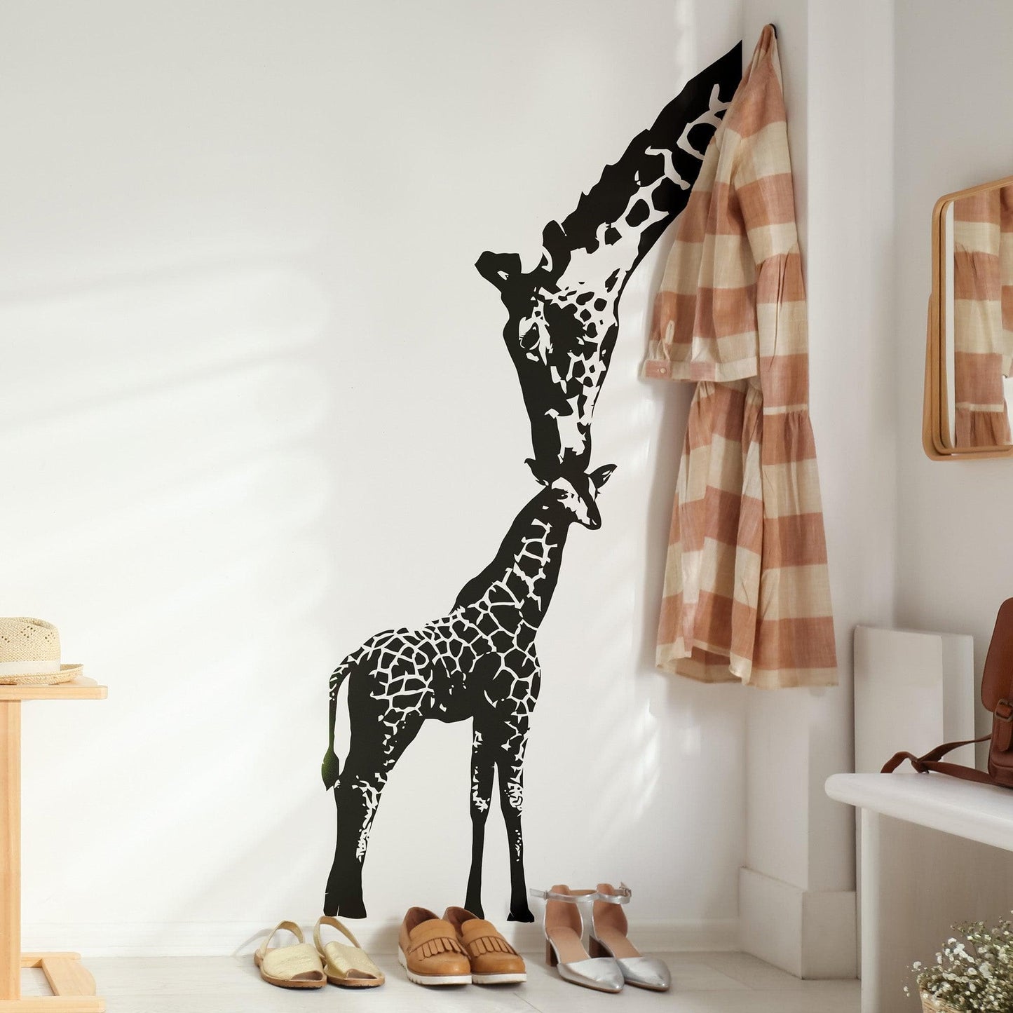 A black adult giraffe and a young giraffe decal on a white wall near shoes and a towel.