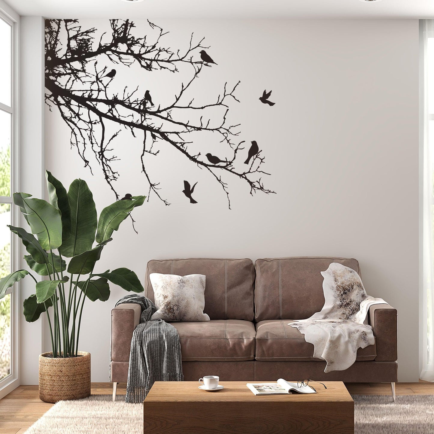 Black decal of 8 birds on tree branches on a white wall above a brown couch and leaves.