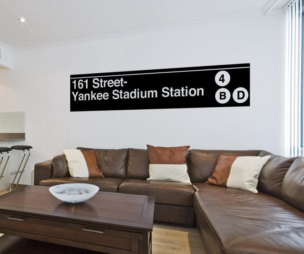 A black decal of a street sign saying "161 Street-Yankee Stadium Station" on a white wall above a brown couch.
