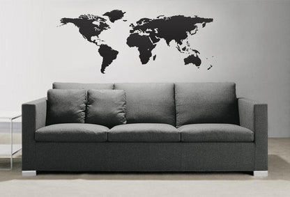 Black world map decal on a white wall above a gray couch.