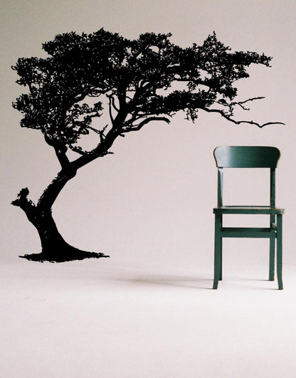 Black tree decal on a white wall next to a green chair.