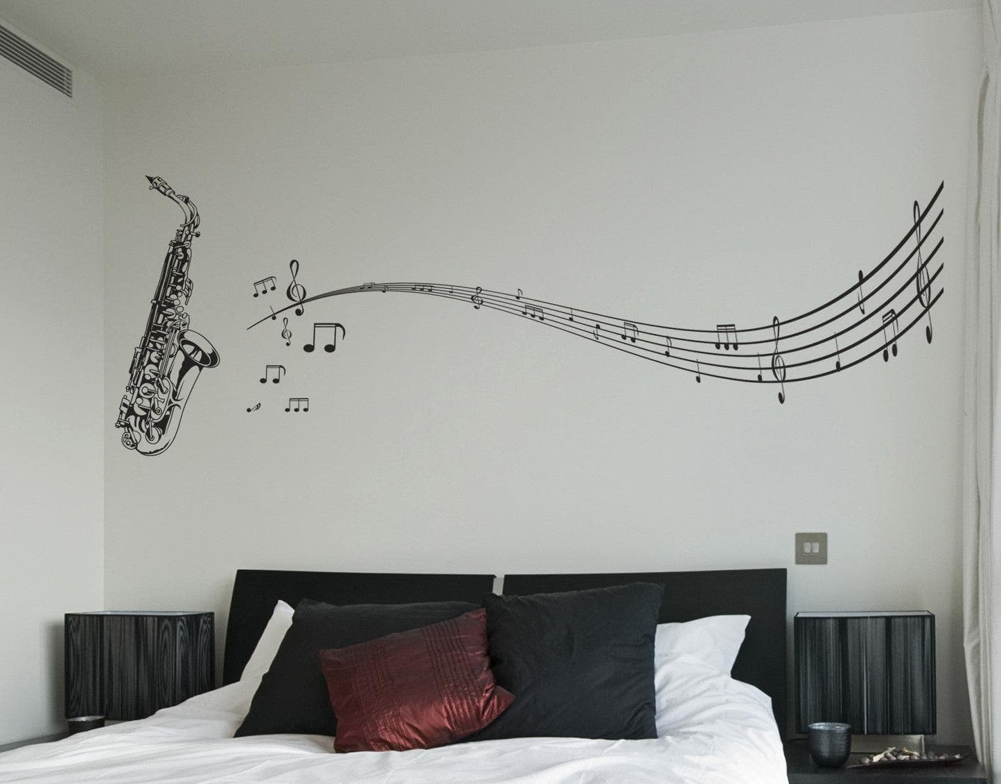 A black decal of a saxophone with musical notes on a white wall above a bed.