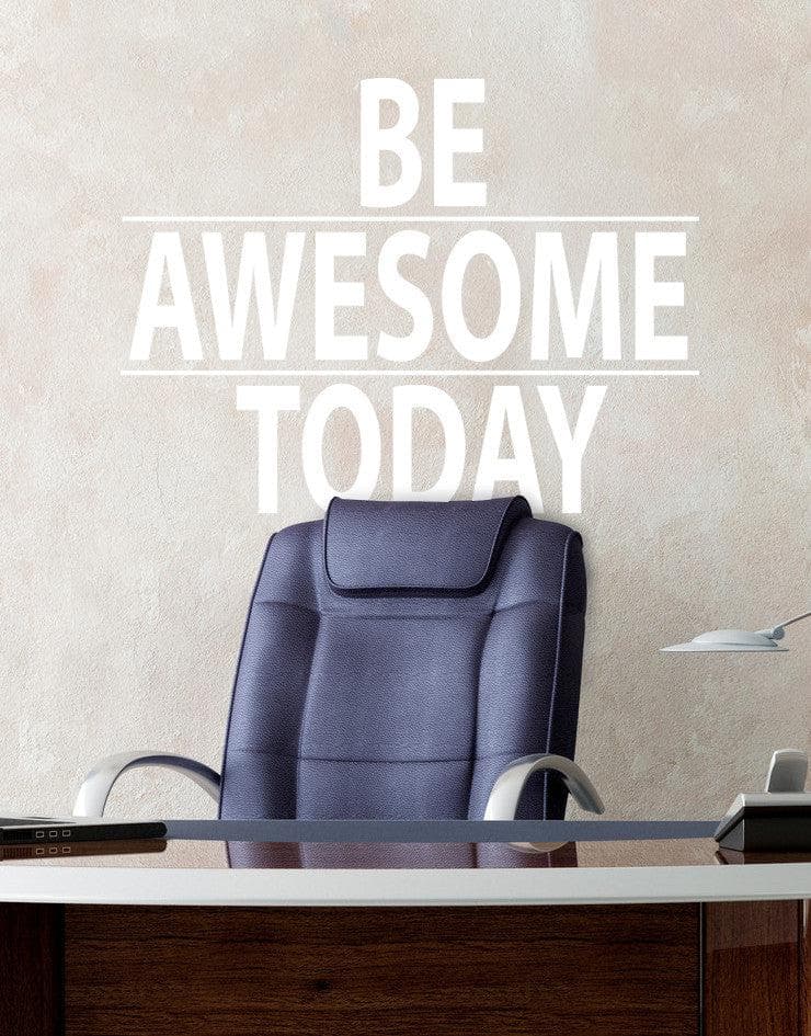 A white text decal saying "BE AWESOME TODAY" on a gray wall over a dark office chair.