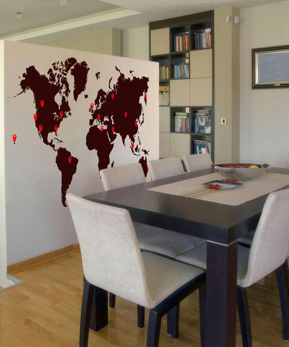 A world map with red pins on various locations against a white wall in a dining room.