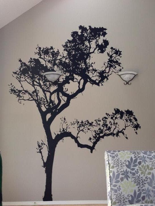 A black tree decal on a white wall near two wall lamps and a couch.