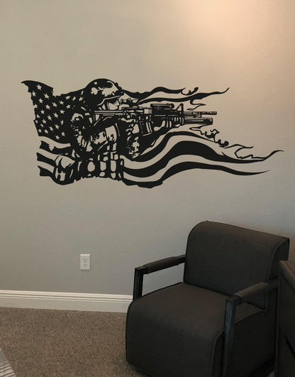 A black decal on a white wall showing a soldier holding a gun and the American flag behind it. Underneath it is a black armchair.