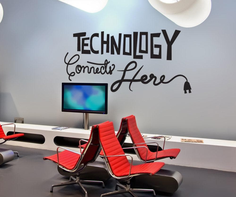 A black decal saying "Technology Connects Here" on a white wall in an office room.