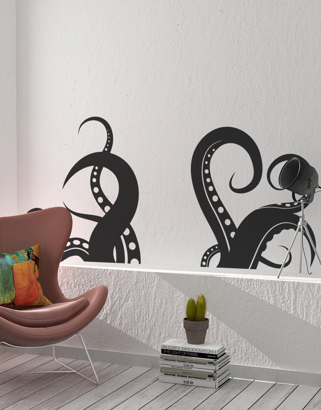 A black octopus tentacles decal on a white wall near an armchair, lamp, and pile of white books with a potted cactus.