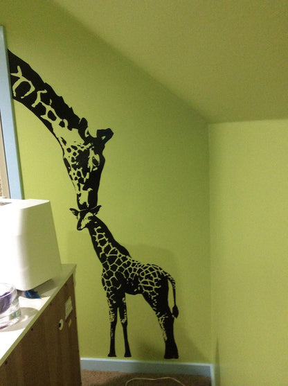 A black adult giraffe and a young giraffe decal on a yellow wall near a cabinet.