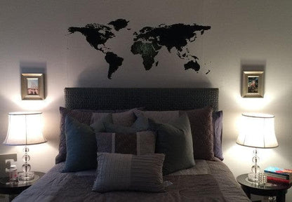 Black world map decal on a white wall above a gray bed.