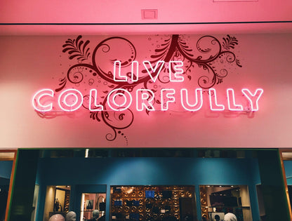 A black floral swirl decal on a white wall behind a neon sign saying "Live colorfully."