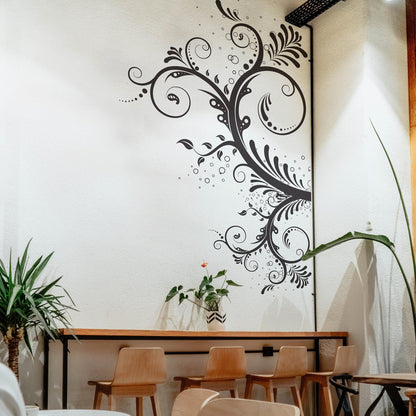 A black large floral swirl decal on a white wall above a desk and 4 chairs.
