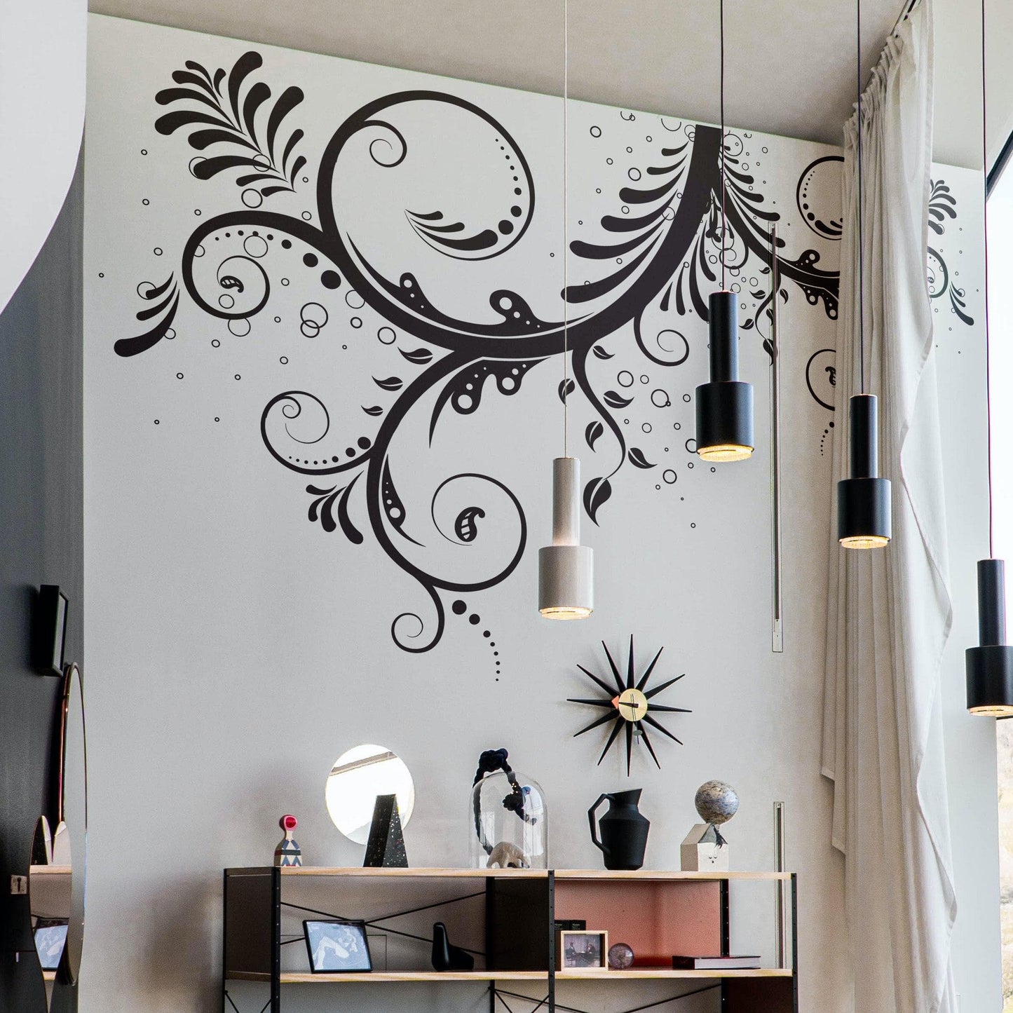 A black floral swirl decal on a white wall above a shelf.