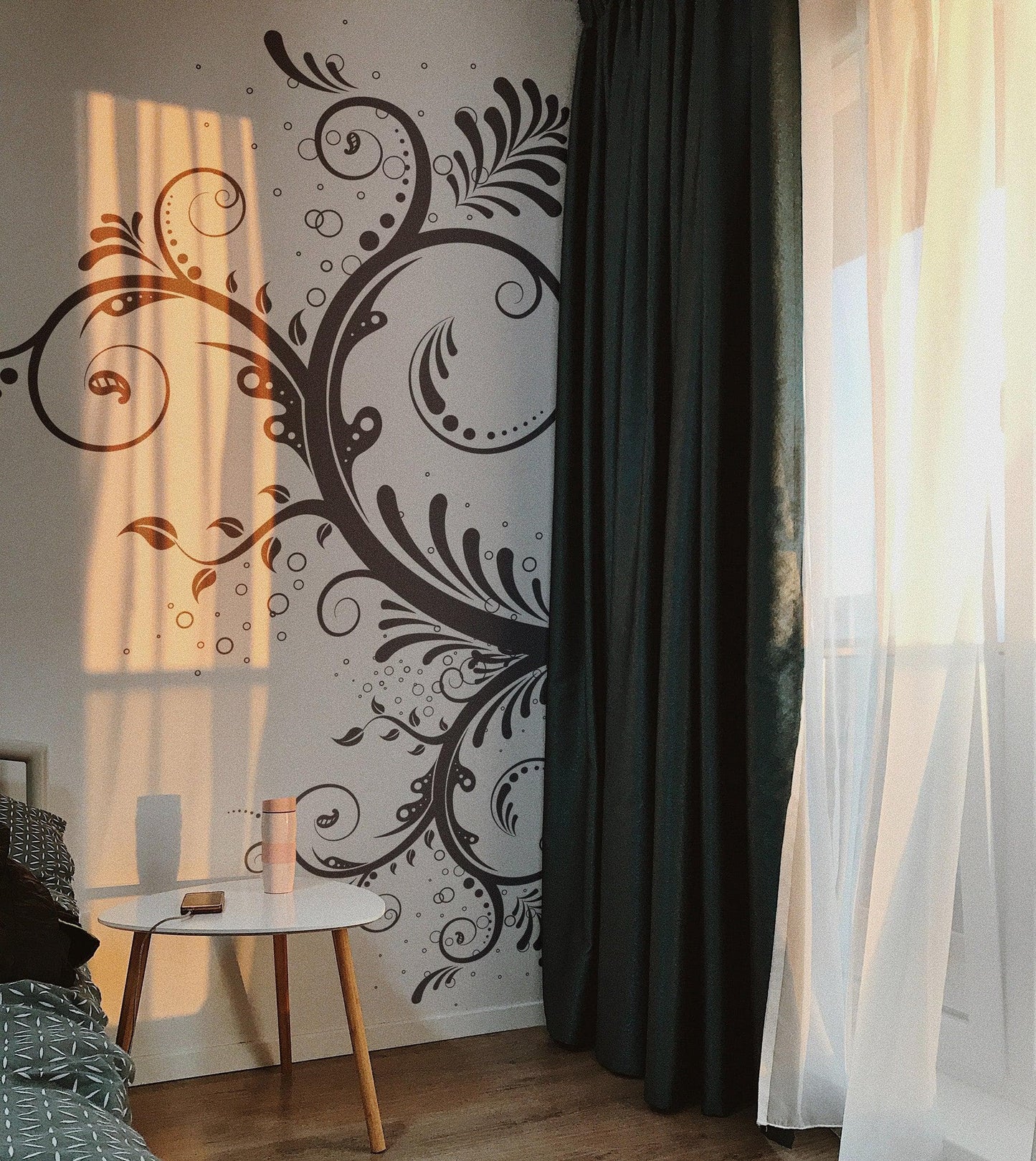 A black floral swirl decal on a white wall in a bedroom.