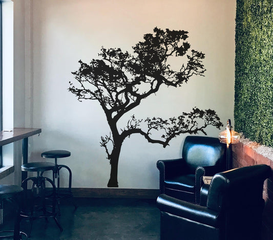 A black tree decal on a white wall near two black armchairs and bar stools. 