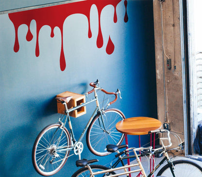 A red decal of slime on a blue wall near two bicycles.