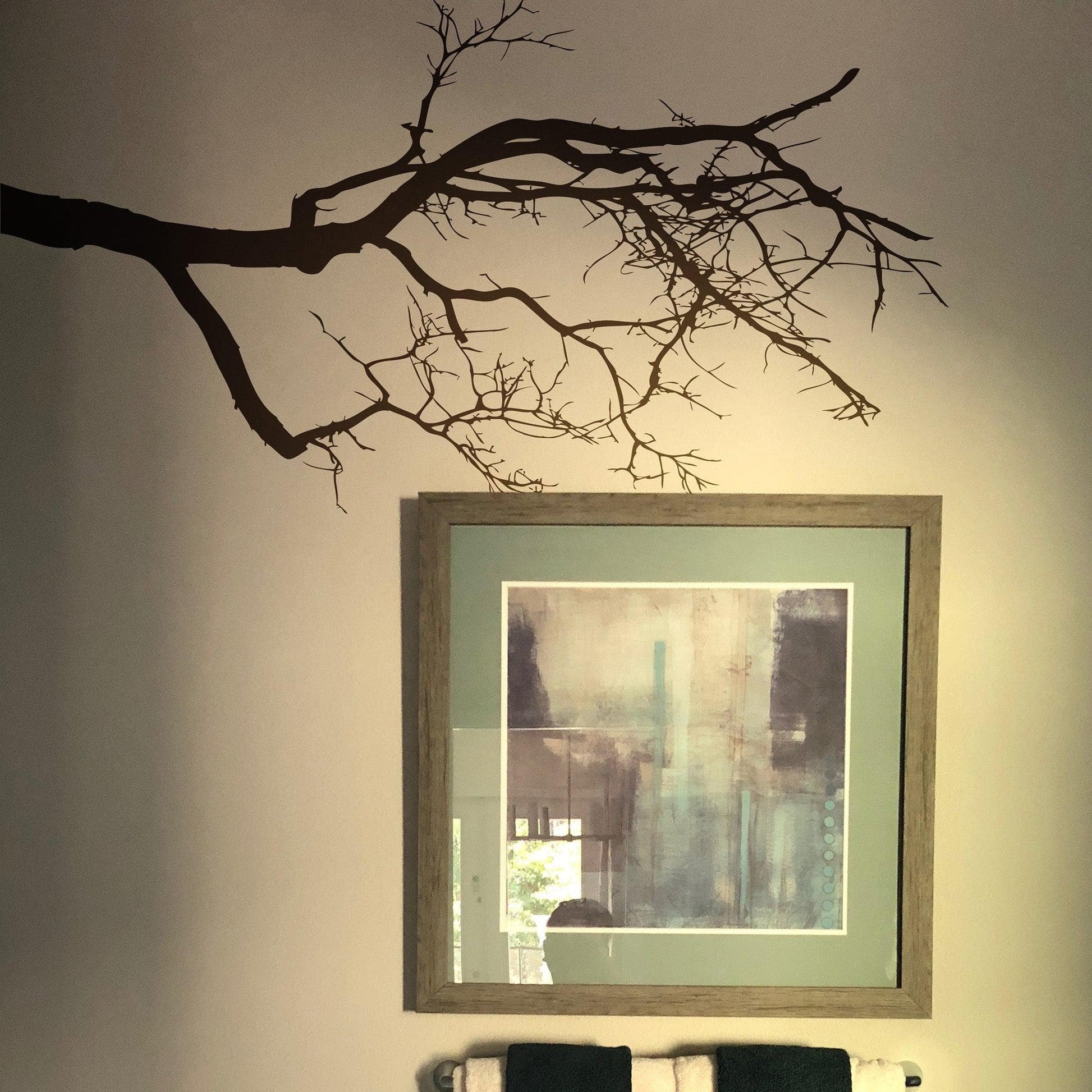 A black decal of tree branches on a white wall near a square photo frame.