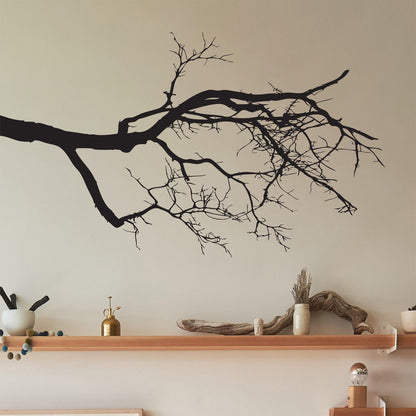 A black decal of tree branches on a white wall above a wooden shelf.