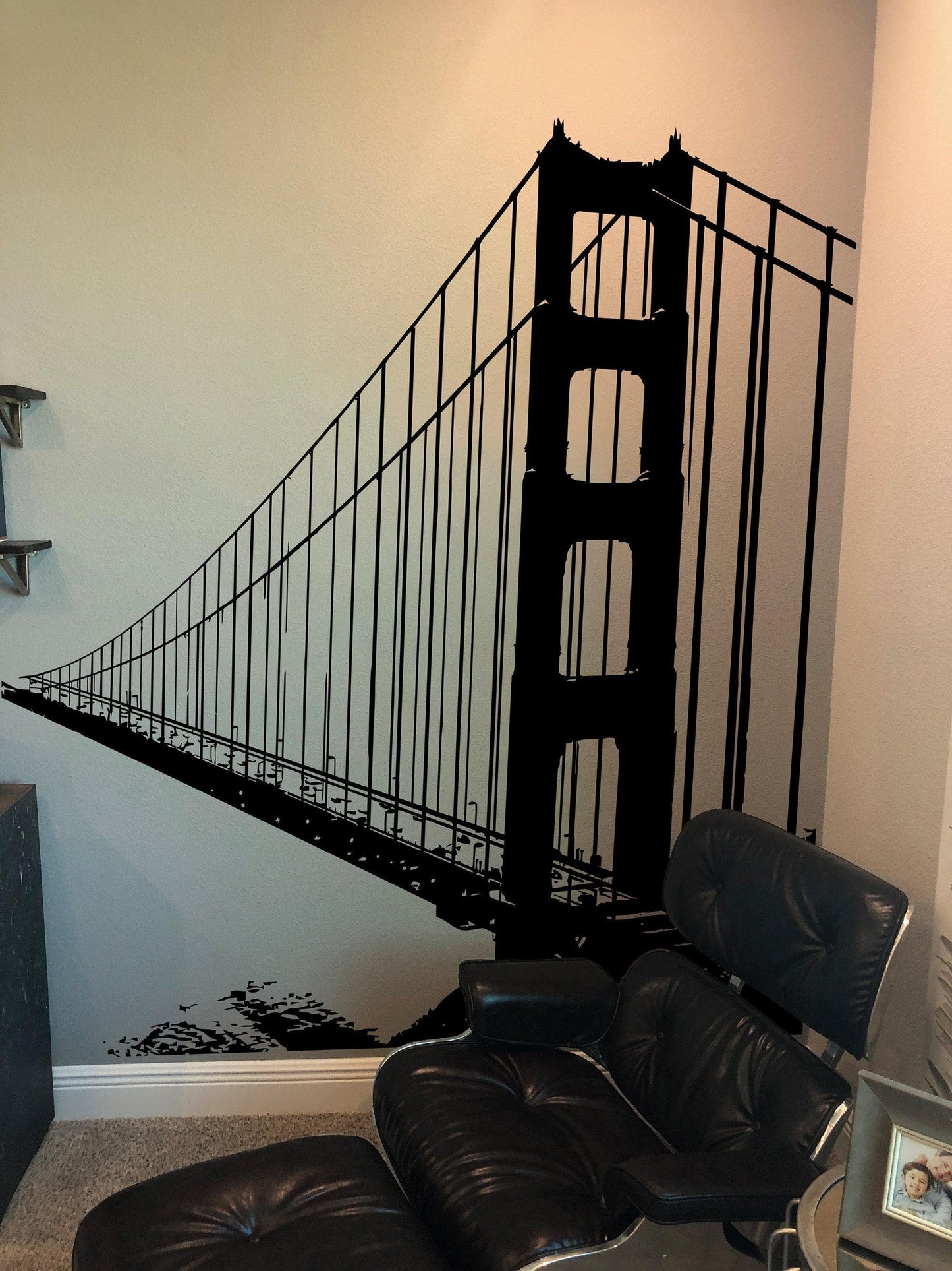 A black decal of the Golden Gate Bridge on a white wall near a black chair.