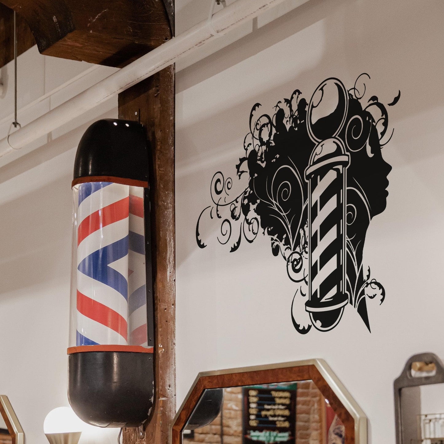 A black decal of a woman silhouette and a barber pole on a white wall near a barber pole and mirror.