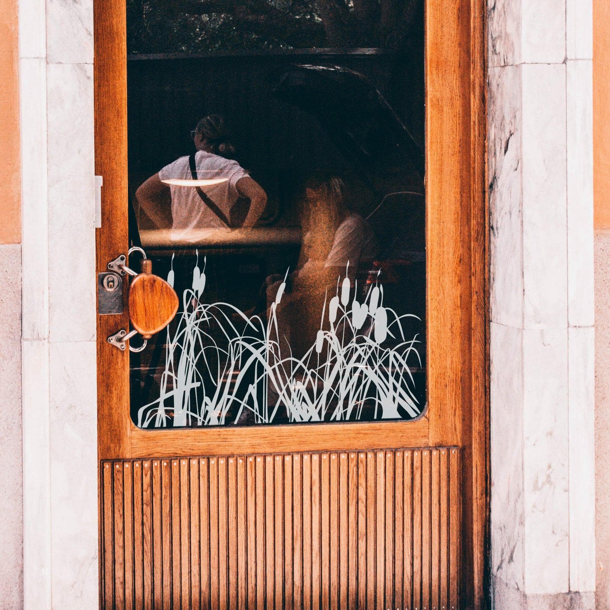 A white cattails decal on a glass window on a door.