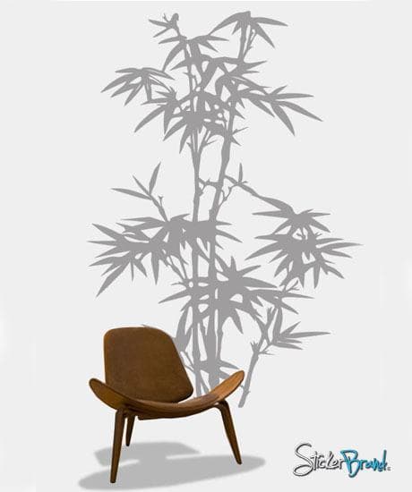 A gray bamboo tree decal on a white wall near a brown chair.