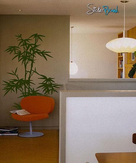 A green bamboo tree decal on a white wall near a red chair and bookshelf.