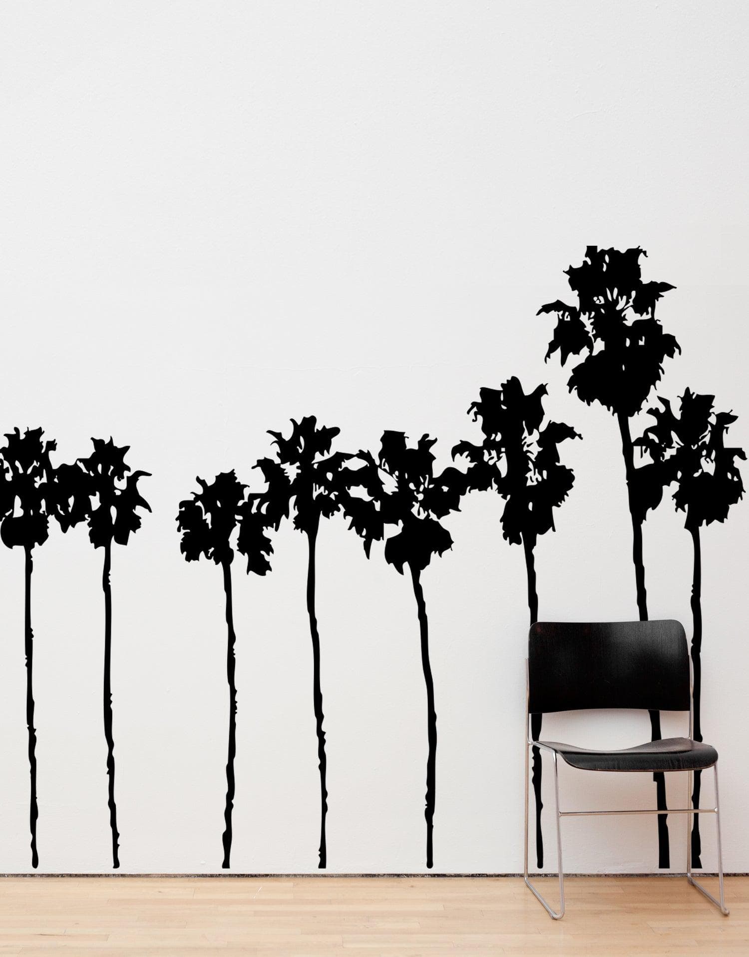 A black decal of a group of palm trees on a white wall near a black chair.