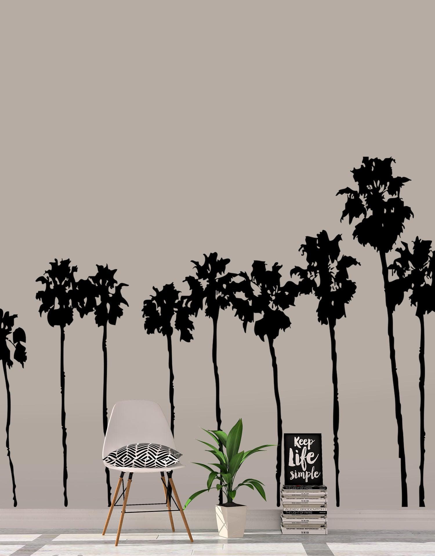 A black decal of a group of palm trees on a white wall near a white couch and an indoor plant. 