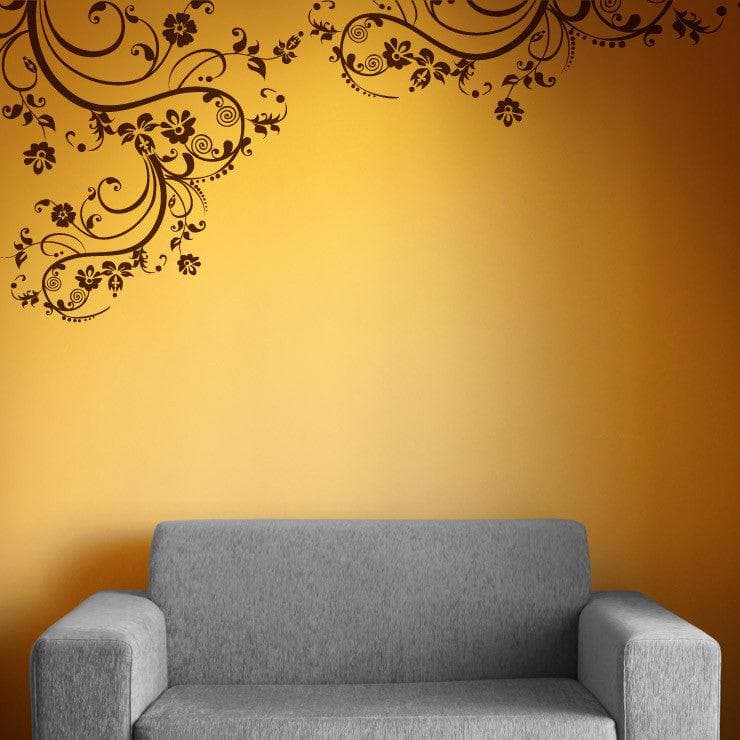 Brown swirling floral decals on a yellow wall above a gray couch.