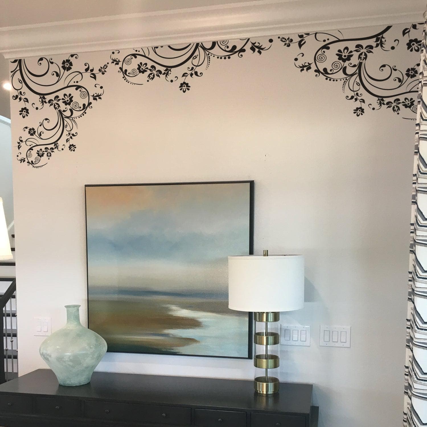 Black floral swirling decals on a white wall above a framed painting.