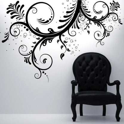 A black floral swirl decal on a white wall above a black chair.