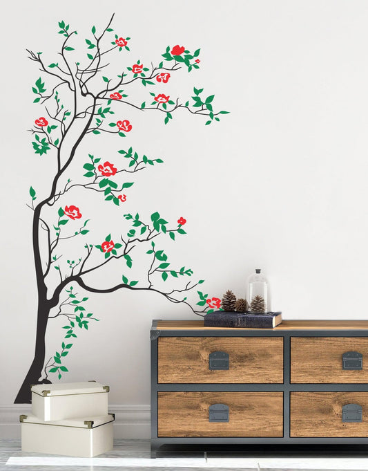 A black tree decal with green leaves and red flowers on a white wall next to a wooden cabinet and two white boxes.