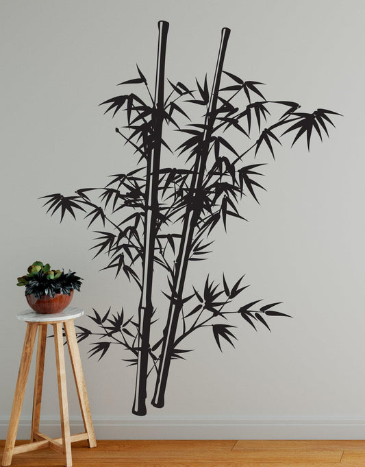 A black decal of a bamboo tree on a white wall near a wooden stone and potted plant.
