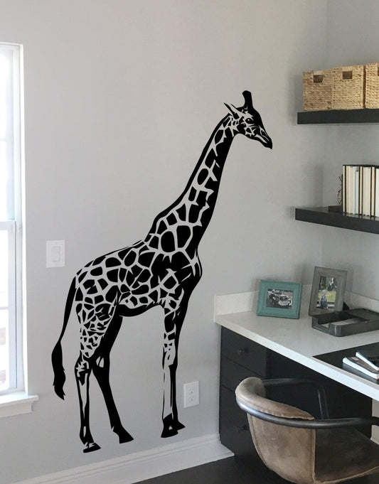 A black decal of a giraffe on a white wall near a desk and shelves.