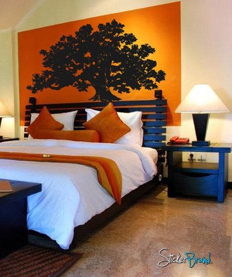 A black tree decal on an orange wall in a bedroom.