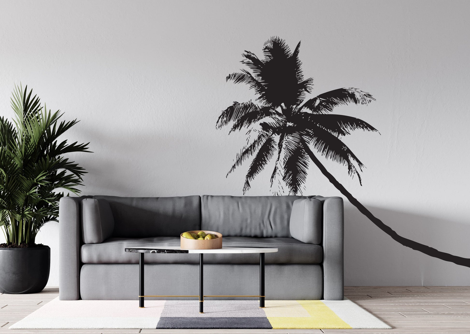 A black coconut tree decal on a white wall near a gray couch.