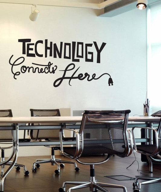 A black decal saying "Technology Connects Here" on a white wall in an office room.